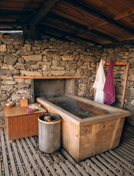 Steinhaus mit rustikalem Holzzuber im Badezimmer, eingebettet in natürliche Materialien und warme Töne.