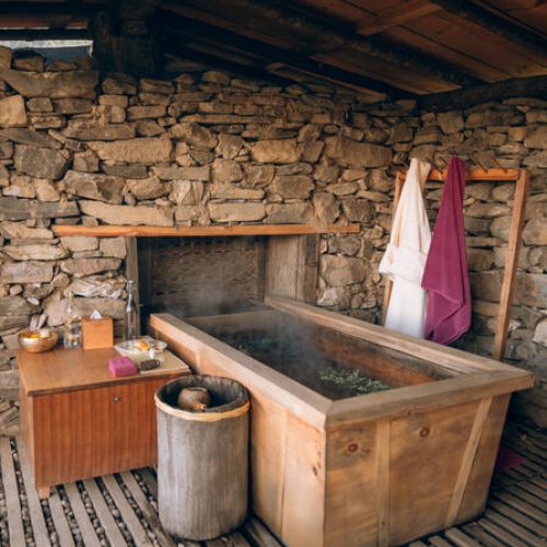 Steinhaus mit rustikalem Holzzuber im Badezimmer, eingebettet in natürliche Materialien und warme Töne.