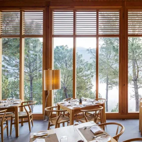 Eleganter Sitzbereich mit Sessel und Couchtisch vor raumhohen Fenstern mit Ausblick ins Grüne